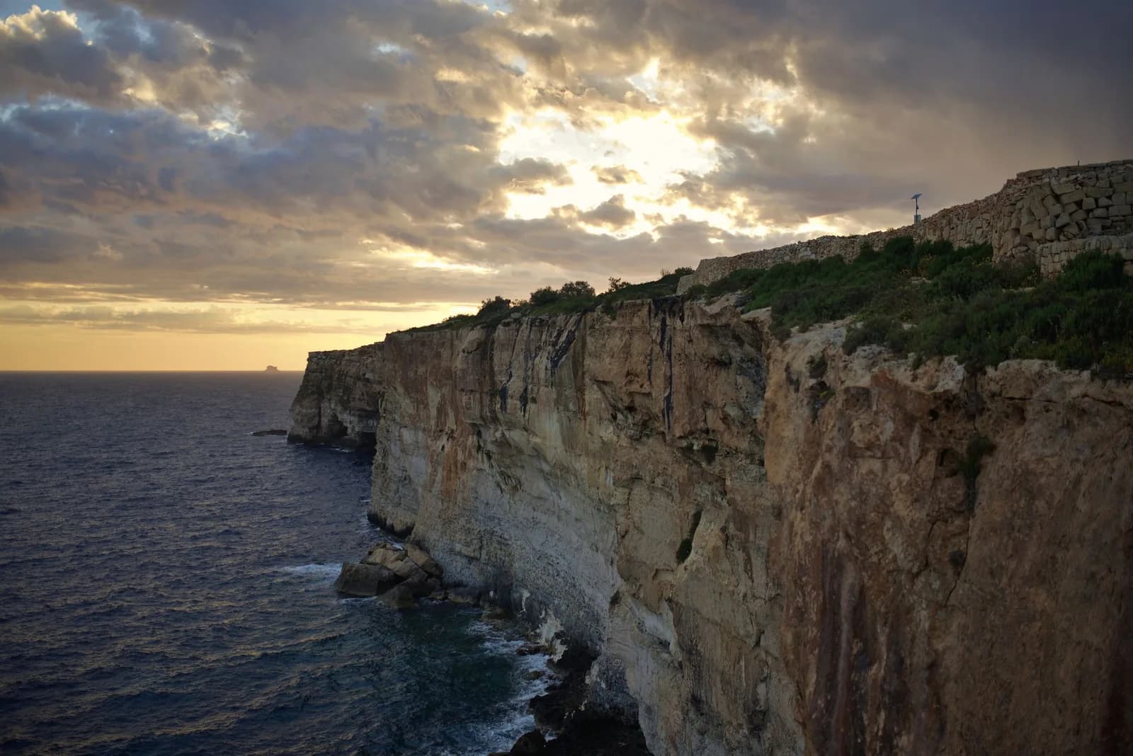 Falaises calcaires à pic de Dingli au coucher du soleil, avec la mer sombre et l'îlot de Filfla à l'horizon