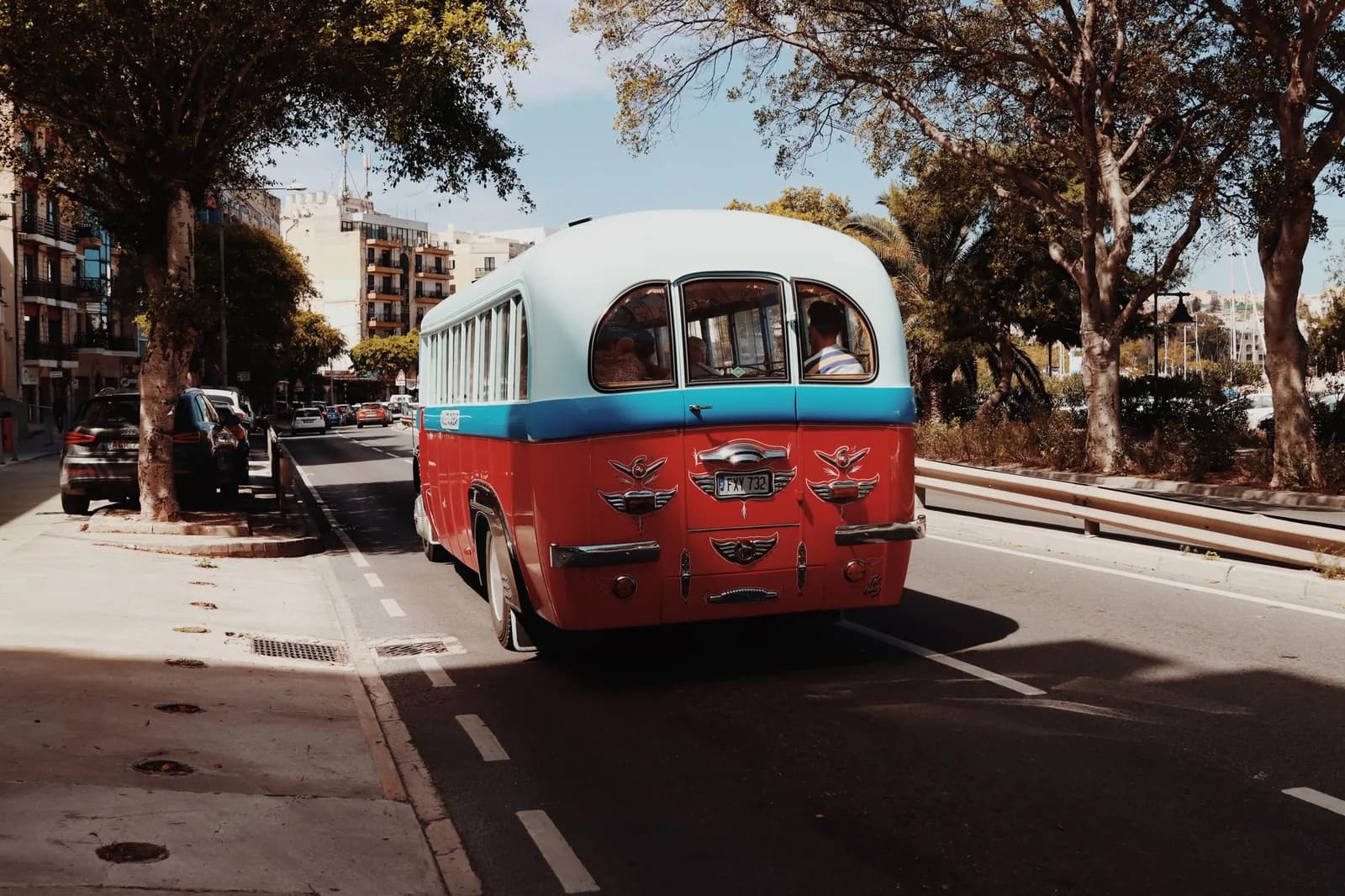 Bus maltais rouge et blanc roulant dans une avenue bordée d'arbres à La Valette