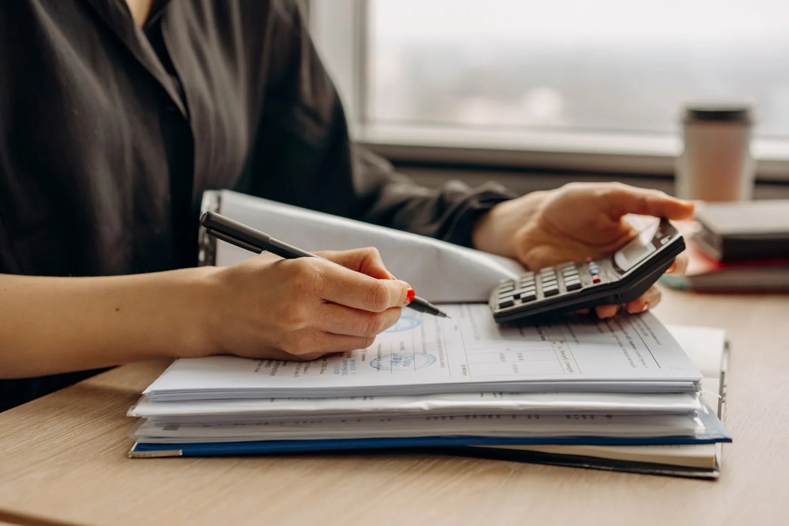 Mains utilisant une calculatrice au-dessus d'une pile de documents fiscaux