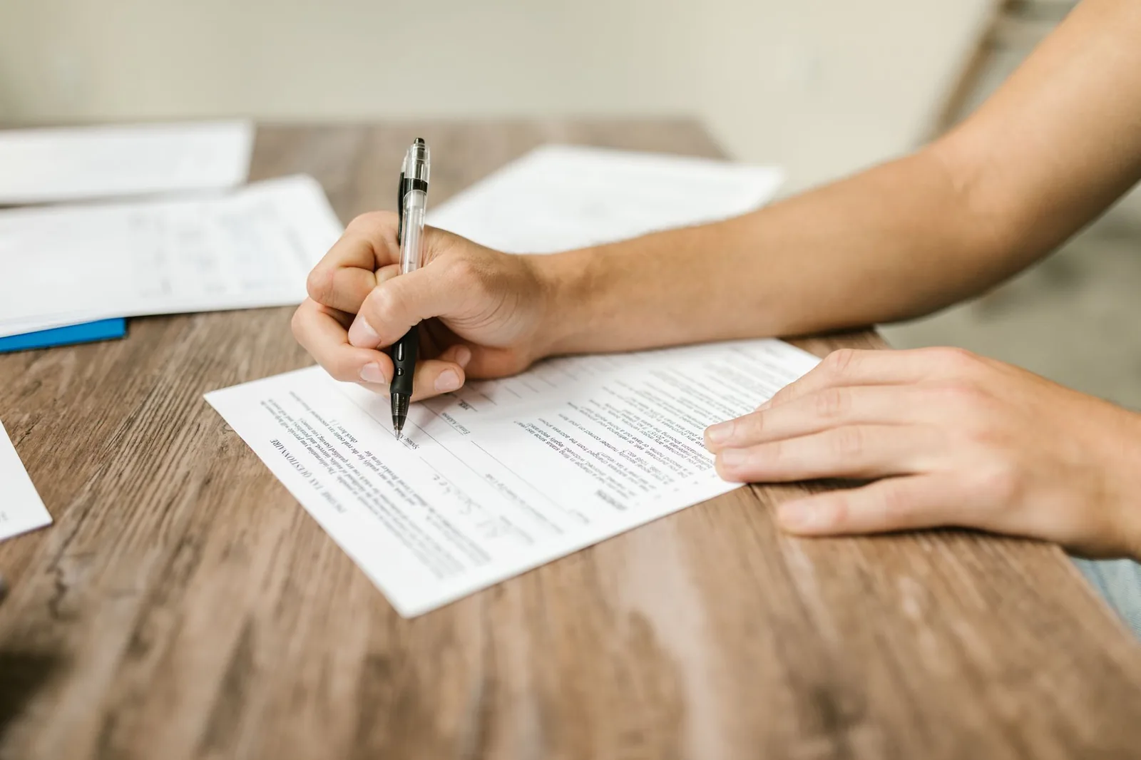 Mains remplissant au stylo un formulaire administratif posé sur une table en bois