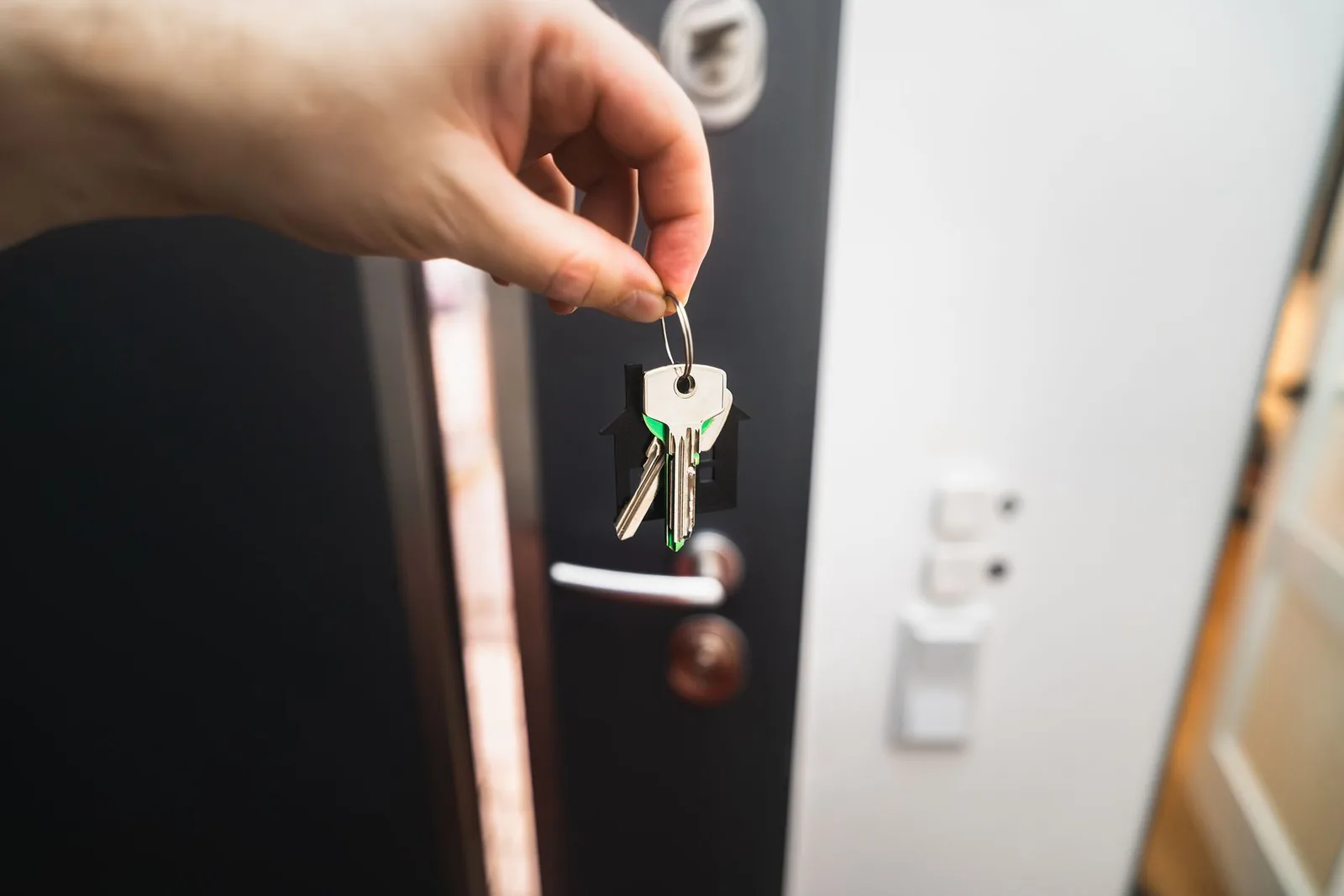 Main tendant un trousseau de clés devant la porte ouverte d'un logement