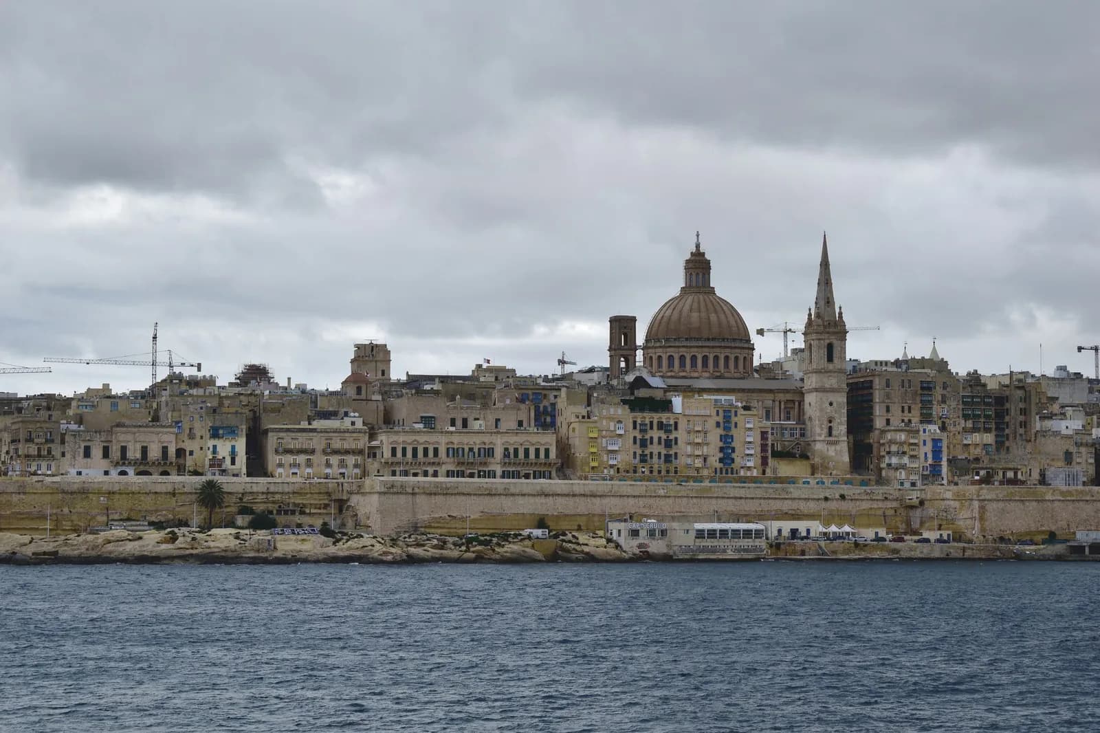 Skyline de La Valette vue de la mer sous un ciel nuageux, avec le dôme de la basilique carmélite et le clocher de la cathédrale anglicane Saint-Paul