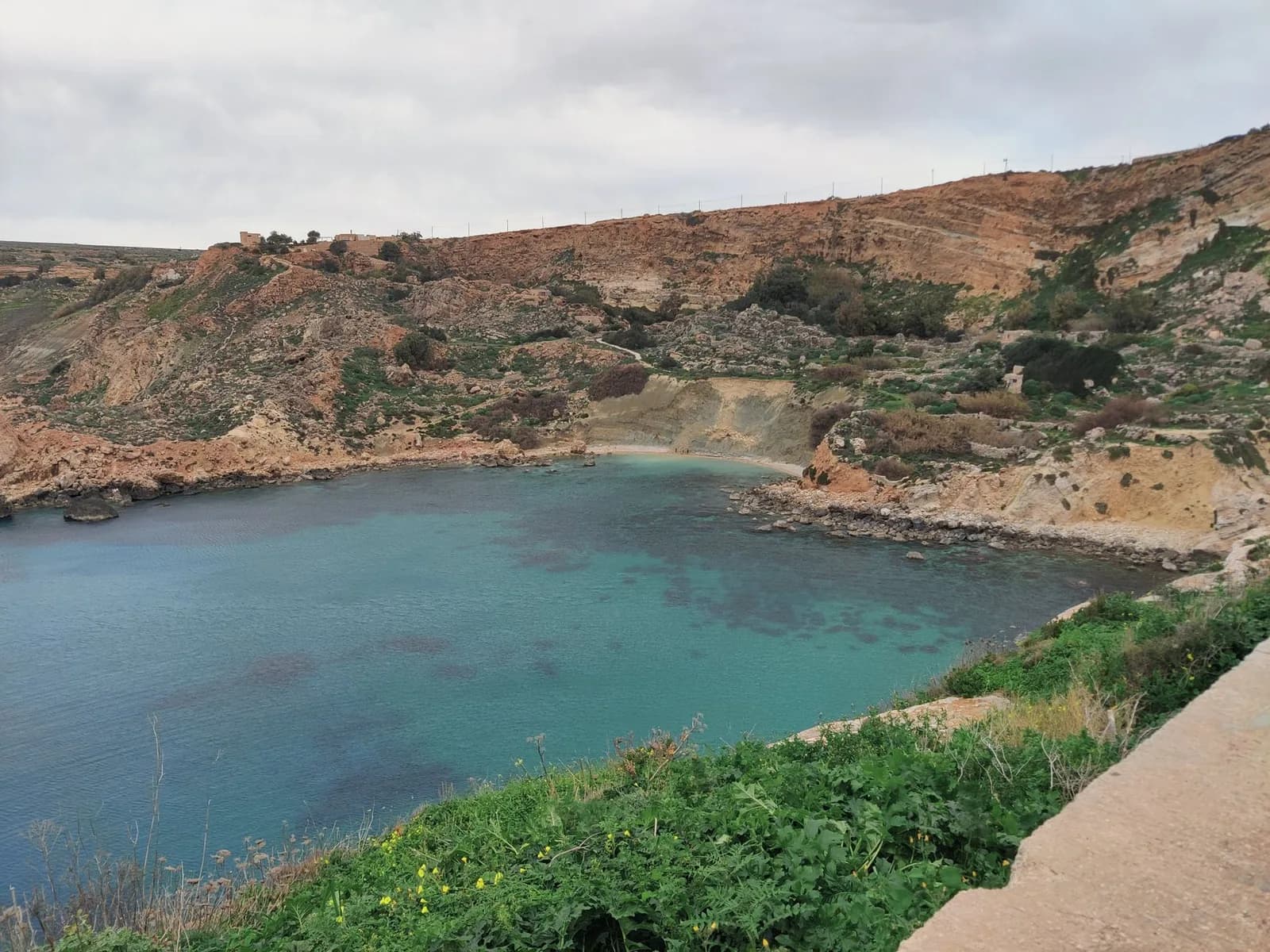 Baie d'eau turquoise entourée de falaises, vue depuis le chemin en surplomb, nord-ouest de Malte