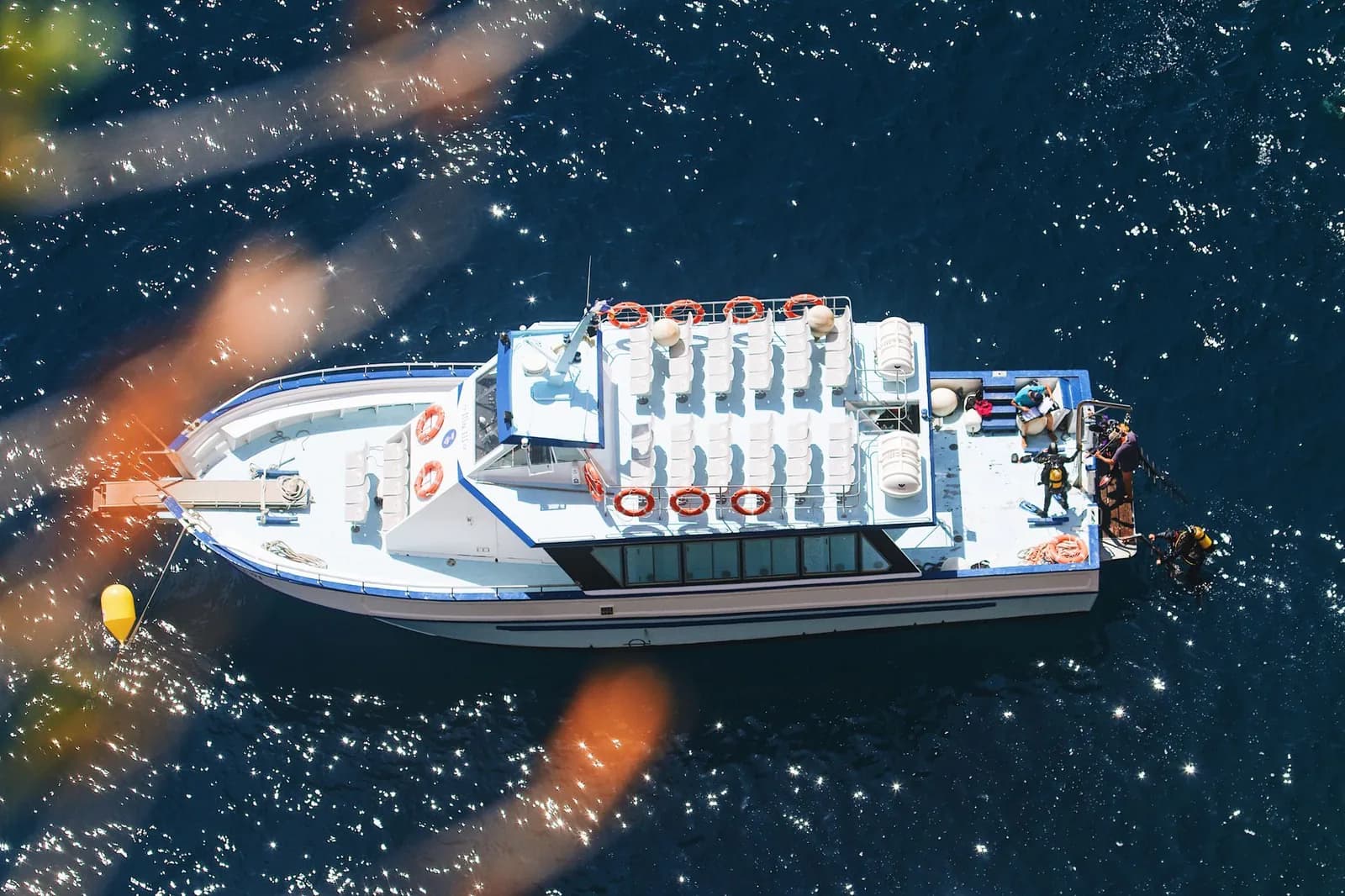 Bateau de plongée vu du dessus, avec des plongeurs équipés de blocs qui se mettent à l'eau, comme lors des sorties vers Comino à Malte