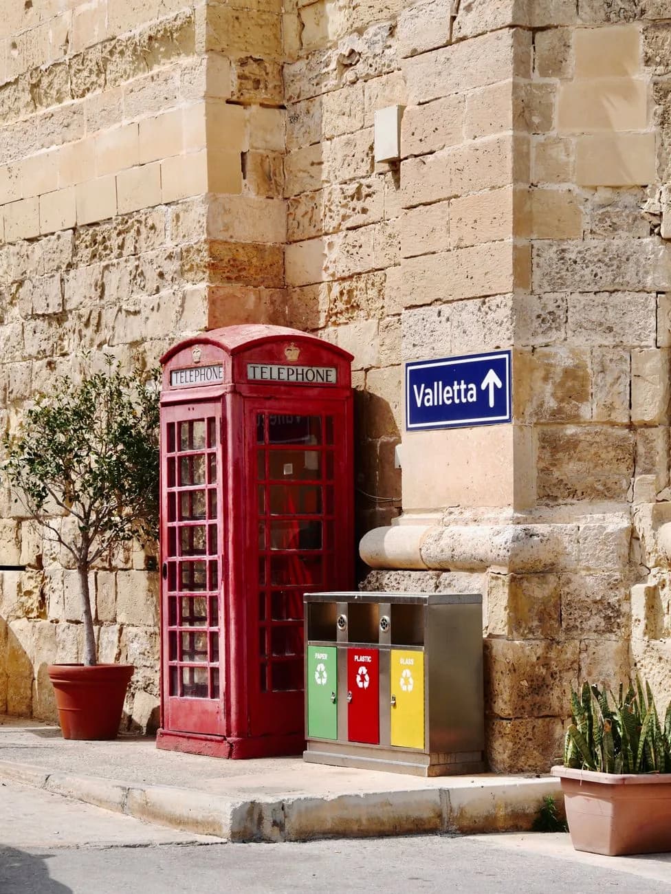 Cabine téléphonique rouge britannique et panneau routier Valletta devant un mur de pierre calcaire, à Malte