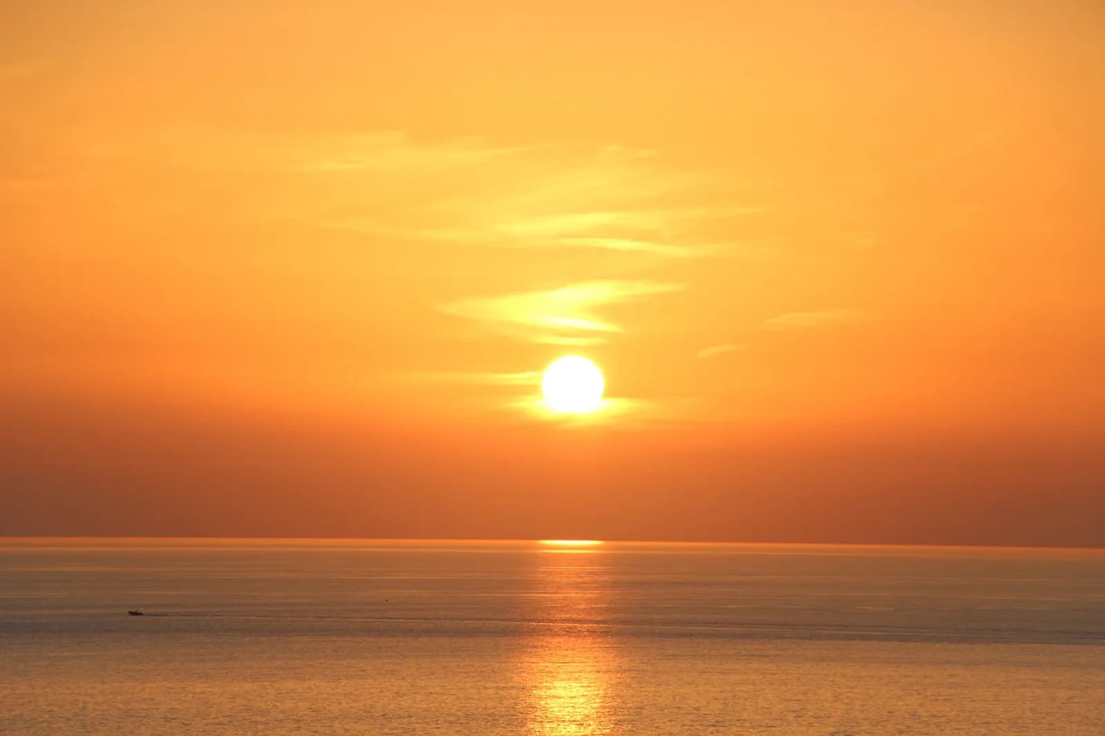 Coucher de soleil orangé sur la mer, avec un petit bateau à l'horizon