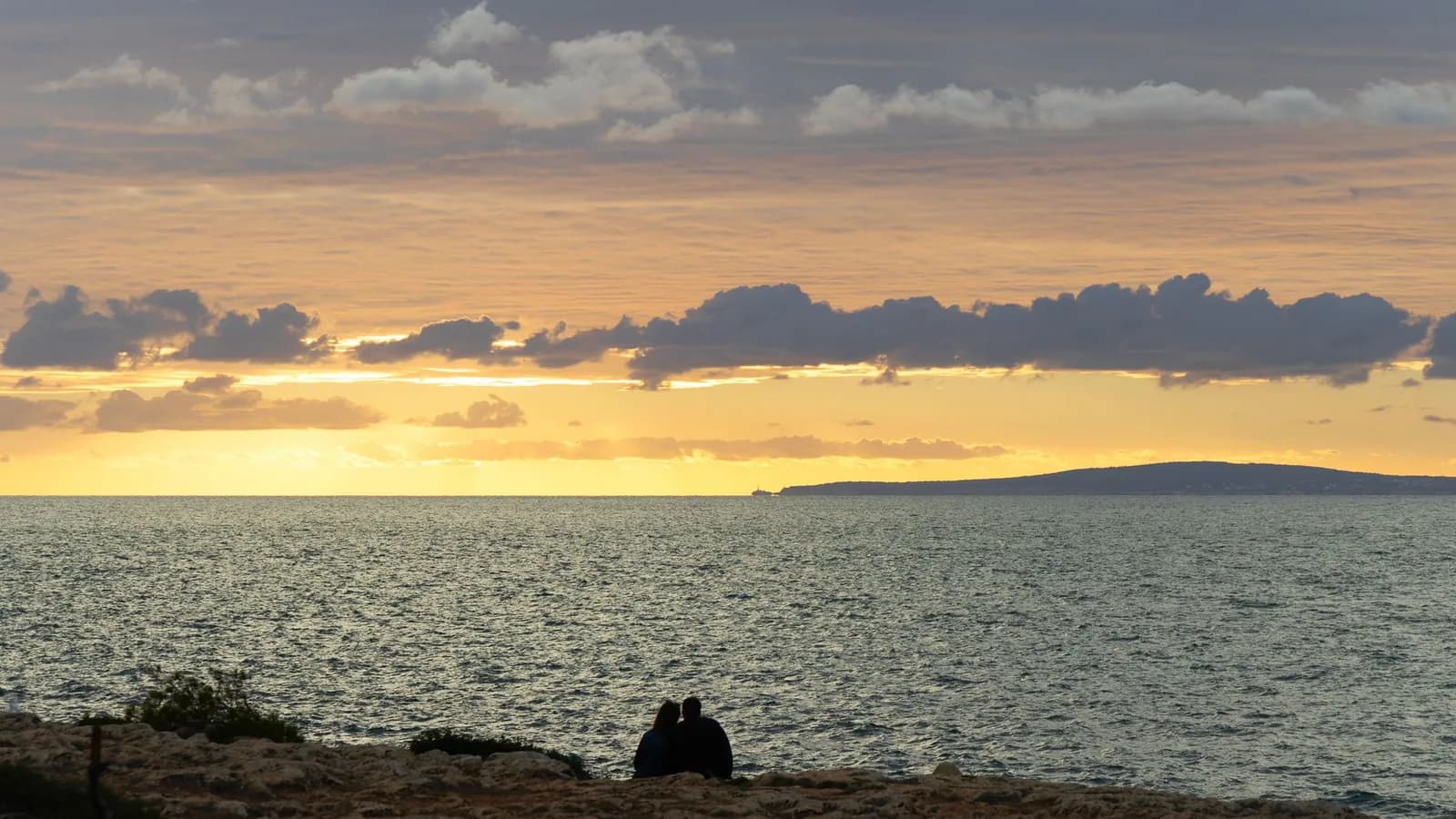 Couple assis au bord de l'eau sur une côte rocheuse de Malte au coucher du soleil