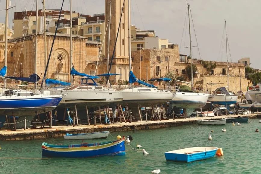 Quai du port de Marsaskala avec voiliers sur cales, barques colorées et clocher en arrière-plan