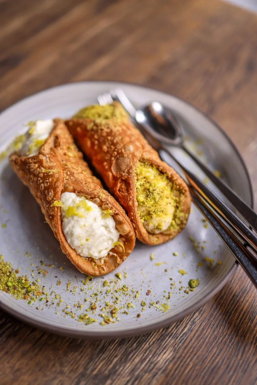 Deux kannoli garnis de ricotta et de pistache concassée sur une assiette, dessert maltais et sicilien