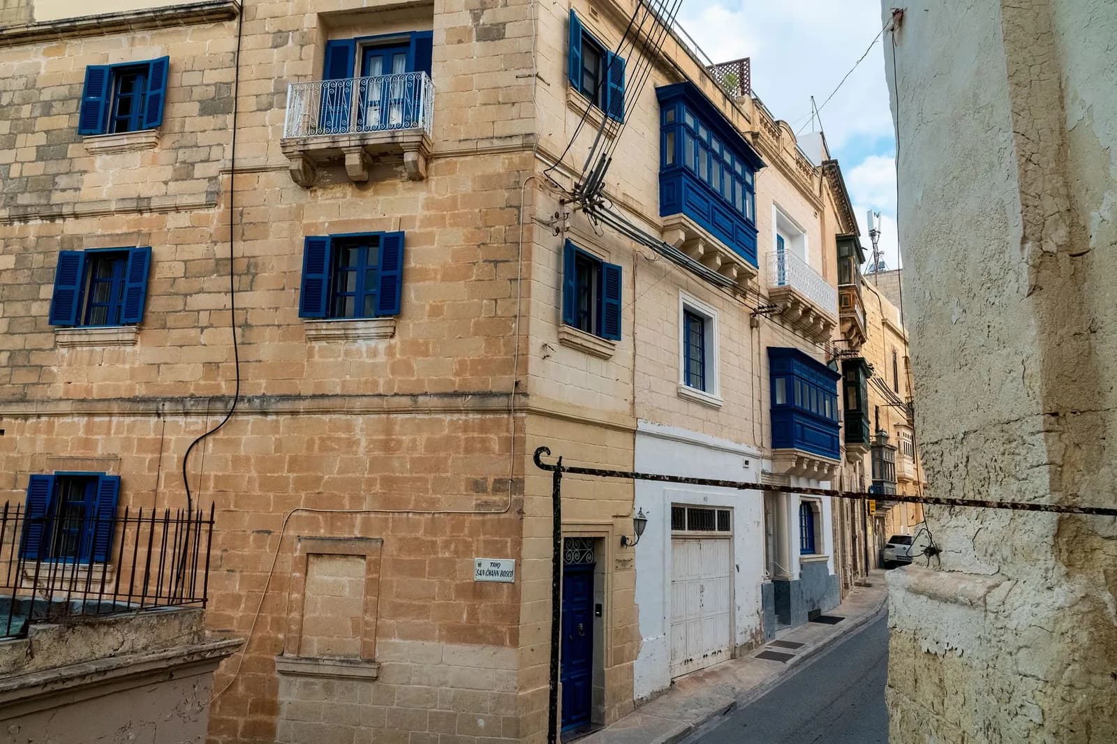 Rue résidentielle maltaise avec maisons en pierre calcaire et balcons fermés bleus typiques