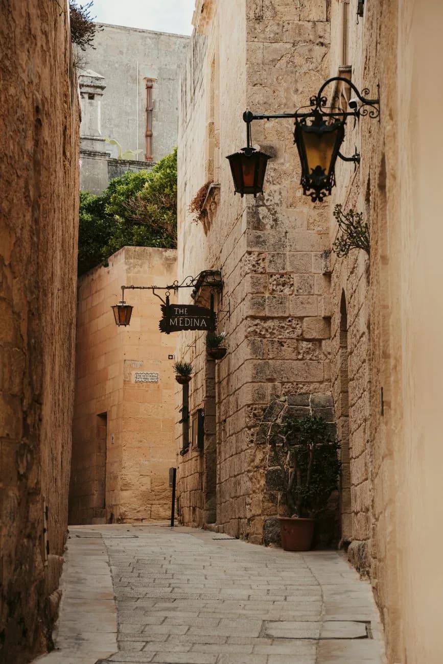 Ruelle pavée en pierre calcaire de Mdina, avec lanternes en fer forgé et plantes en pot