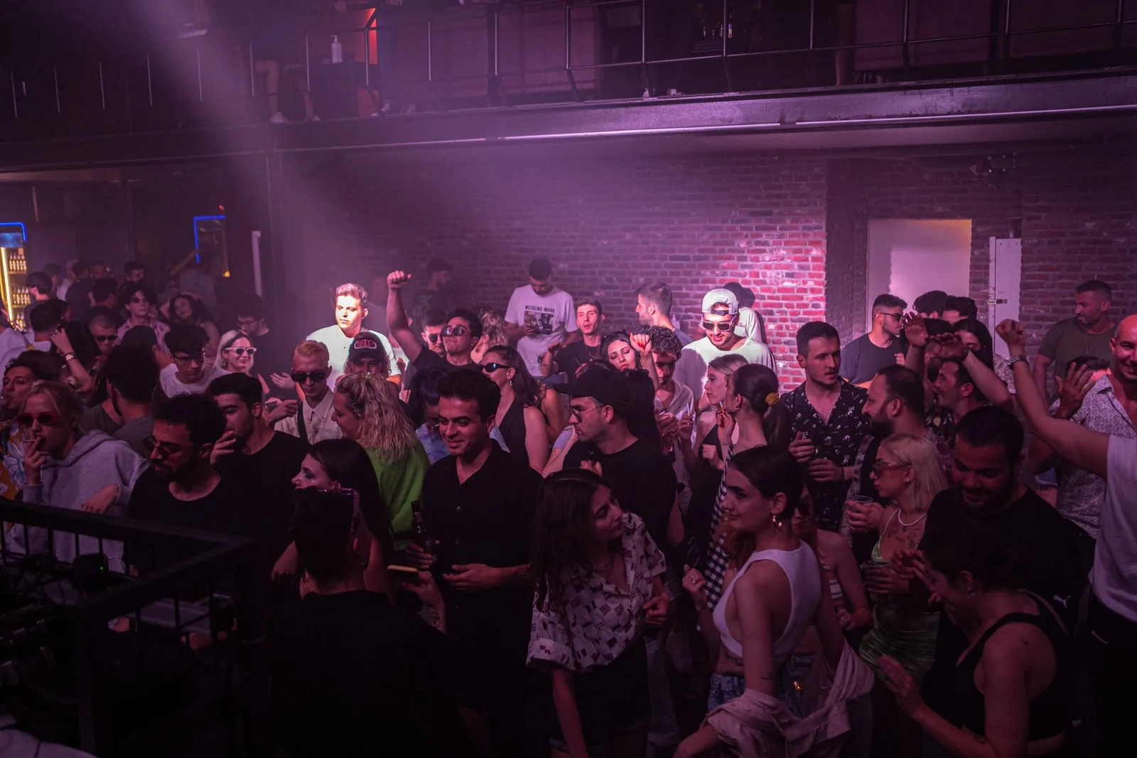 Piste de danse bondée dans une boîte de nuit, éclairée par des projecteurs violets et de la fumée