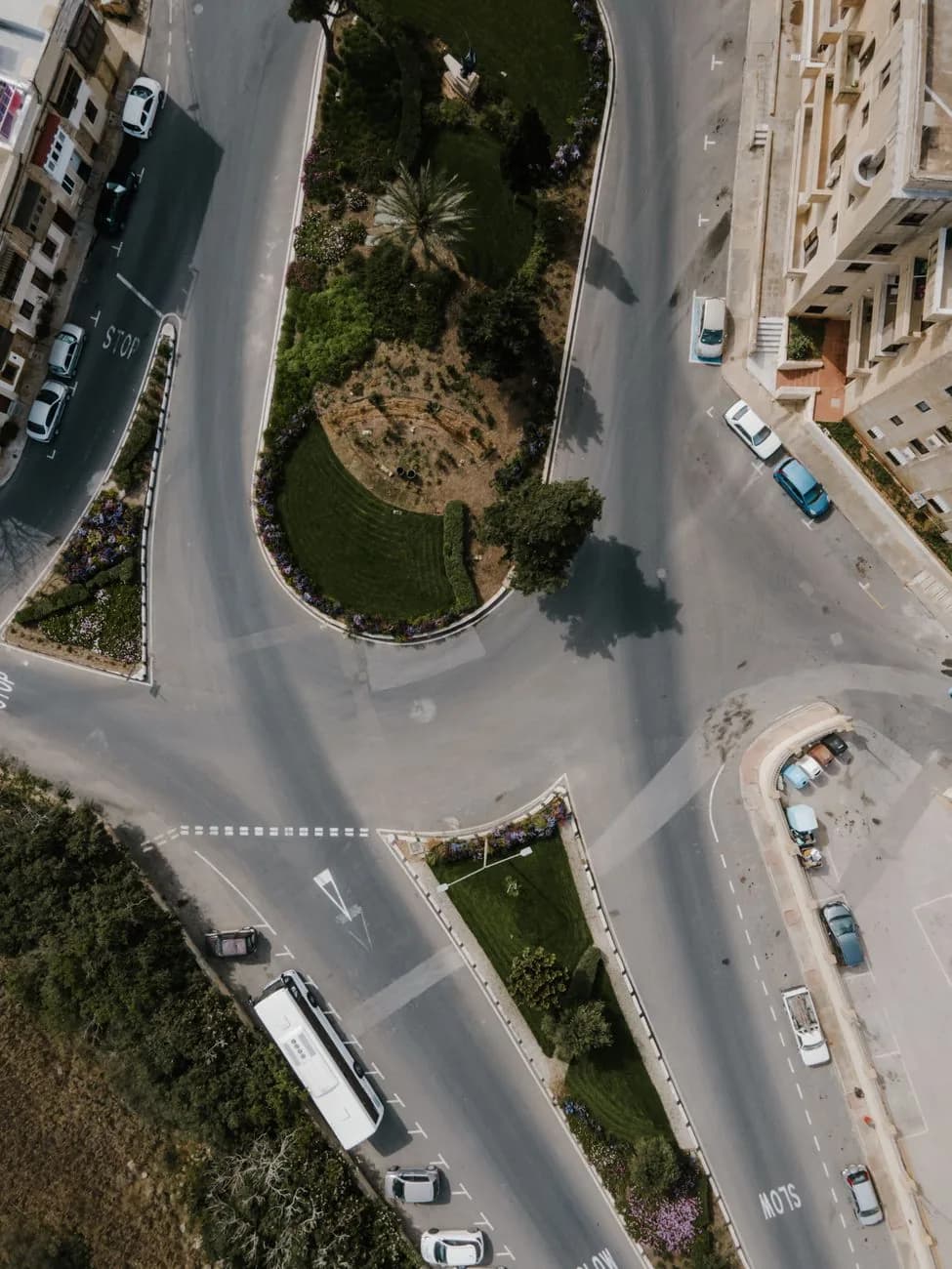 Vue aérienne d'un grand rond-point maltais avec voitures, bus et marquages STOP et SLOW au sol