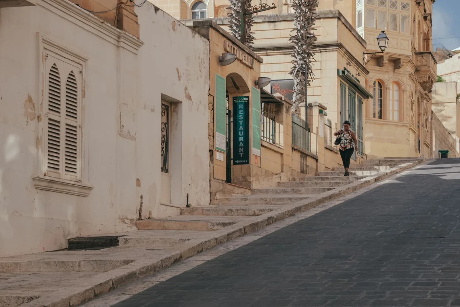 Rue en pente bordée de maisons en pierre calcaire menant à la Citadelle de Victoria, à Gozo
