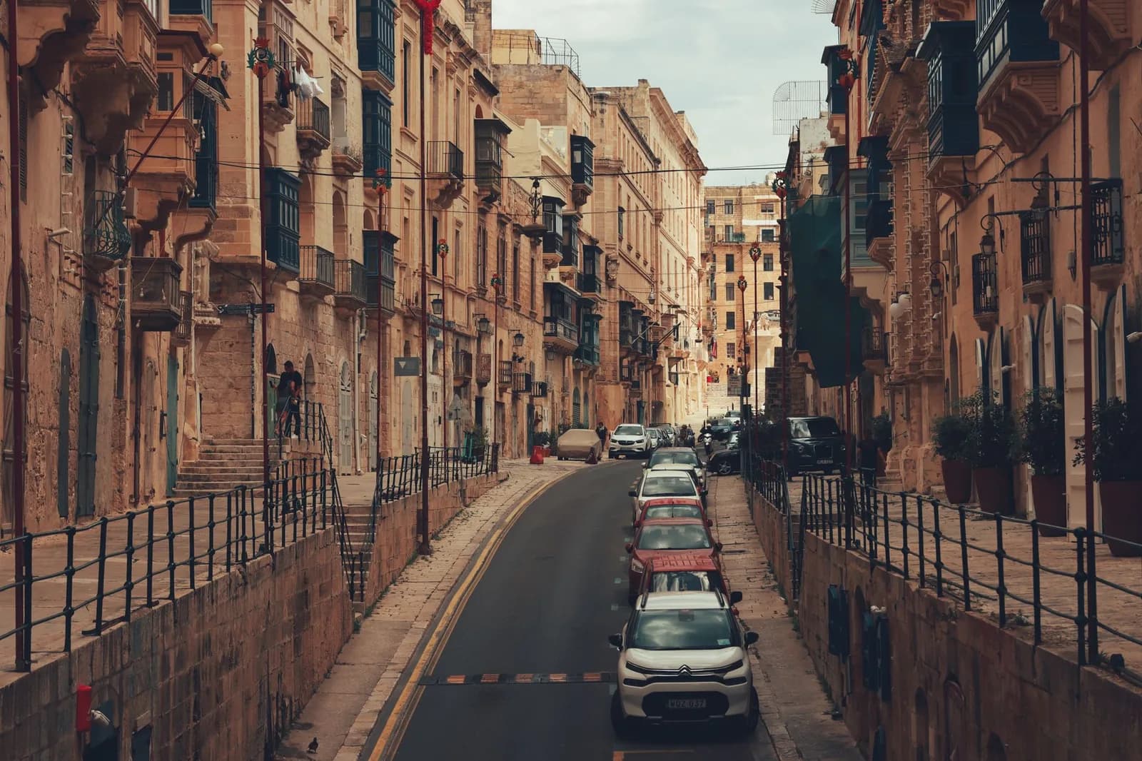 Rue en pente de La Valette bordée de voitures garées, immatriculations maltaises, à Malte