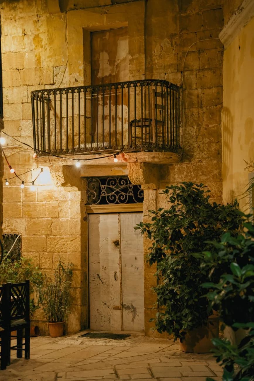 Ruelle en pierre calcaire éclairée le soir, avec un balcon en fer forgé, à Malte