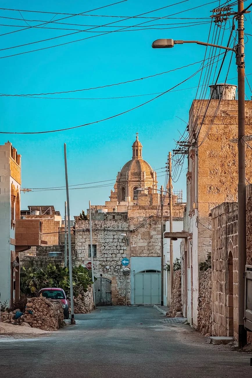 Ruelle calme d'un village de Gozo à Malte, maisons en pierre calcaire et dôme d'église au fond