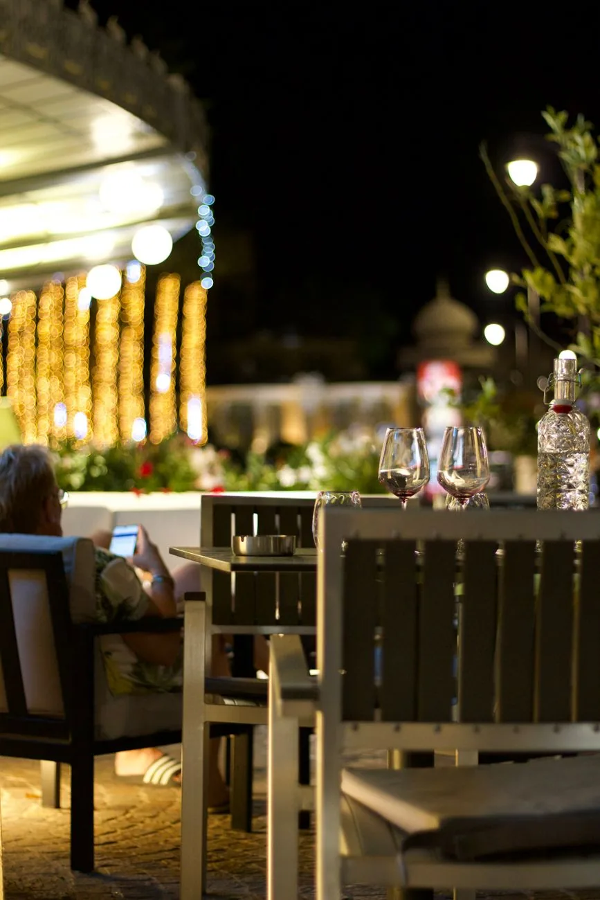 Terrasse de bar méditerranéen le soir, guirlandes lumineuses, verres de vin sur une table en bord de rue