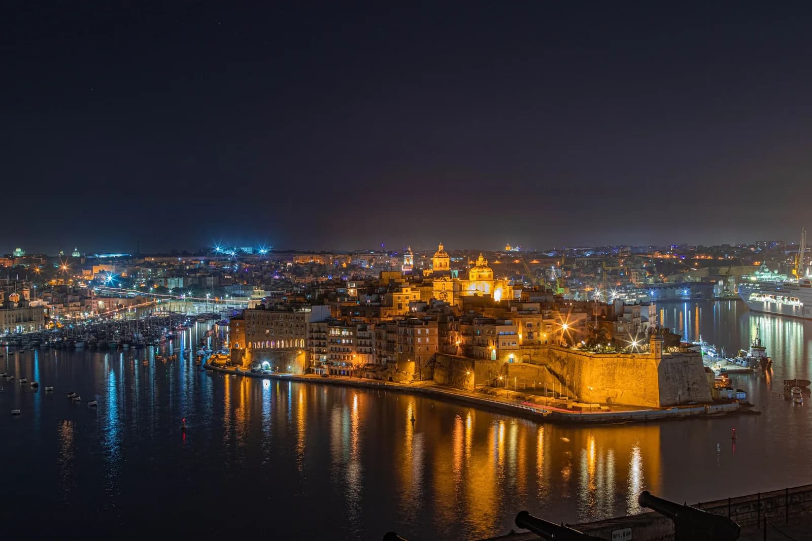 Vue de nuit sur le Grand Harbour et Birgu éclairés, avec le Fort Saint-Ange illuminé et ses reflets dans l'eau